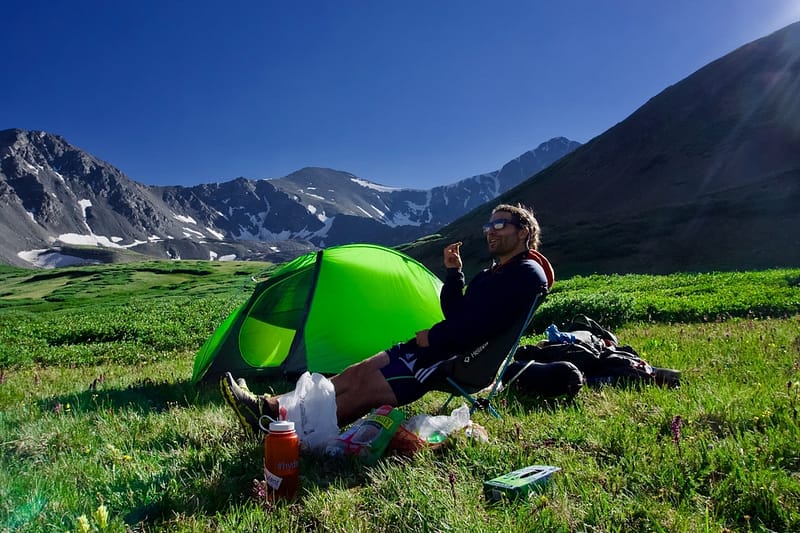 man sitting on camping chair beside green tent